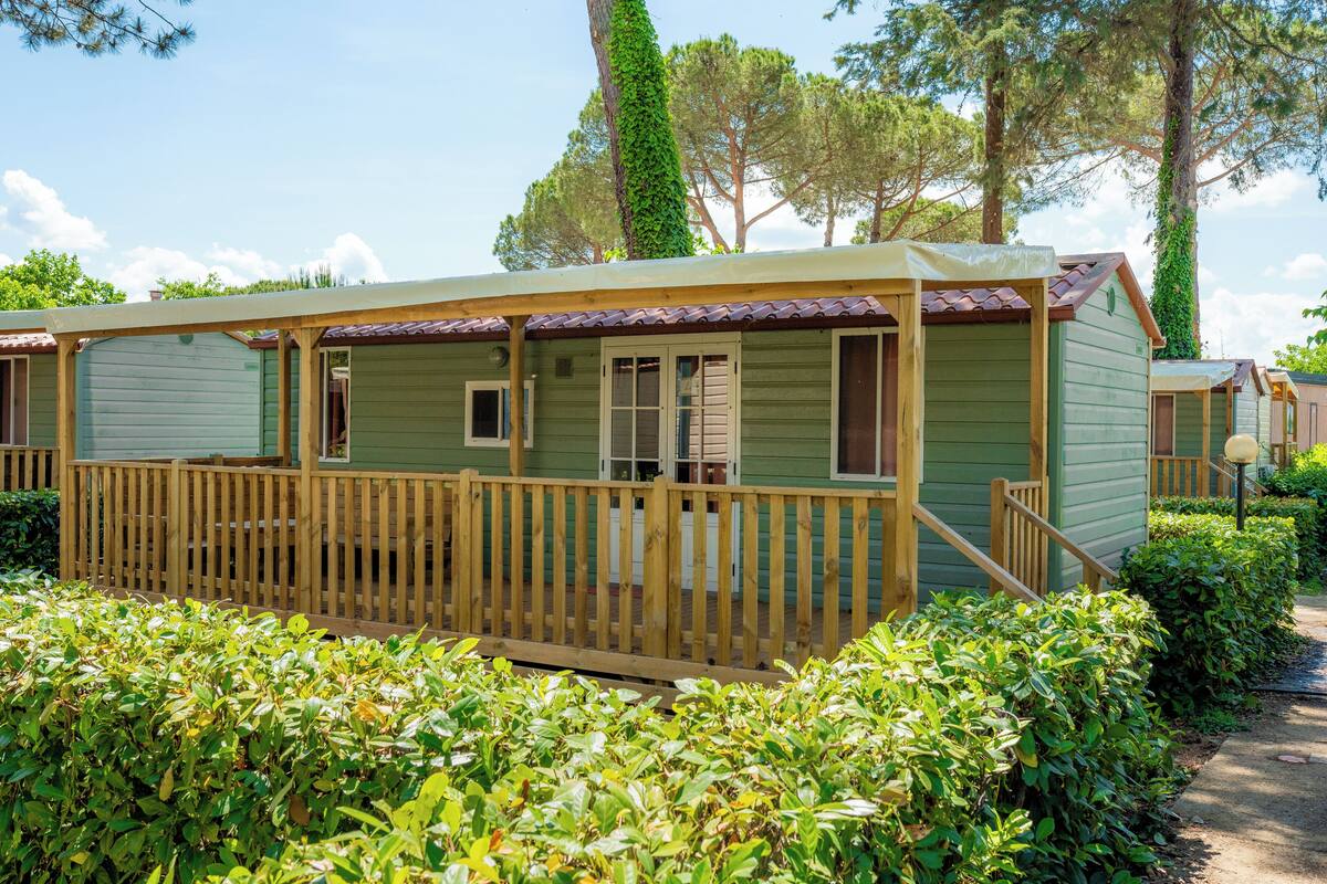 Una hilera de casas móviles verdes con barandillas de madera y un porche cubierto.