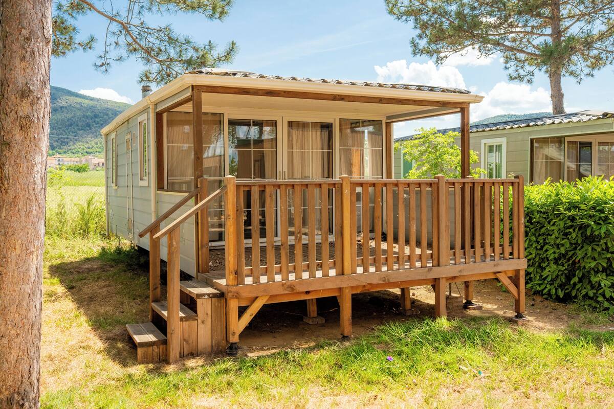 Una terraza de madera con una escalera que lleva a un espacio cubierto con ventanas.
