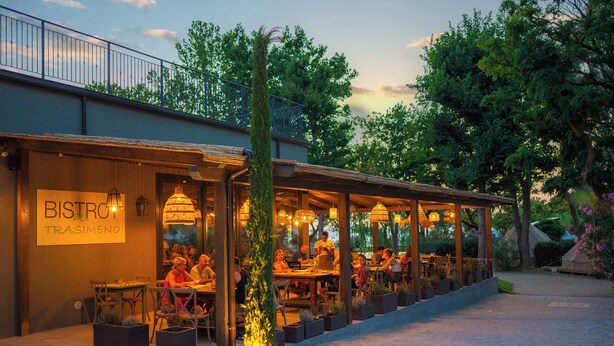 Ein Restaurant im Freien mit Tischen und Stühlen, umgeben von Kübelpflanzen und Bäumen.