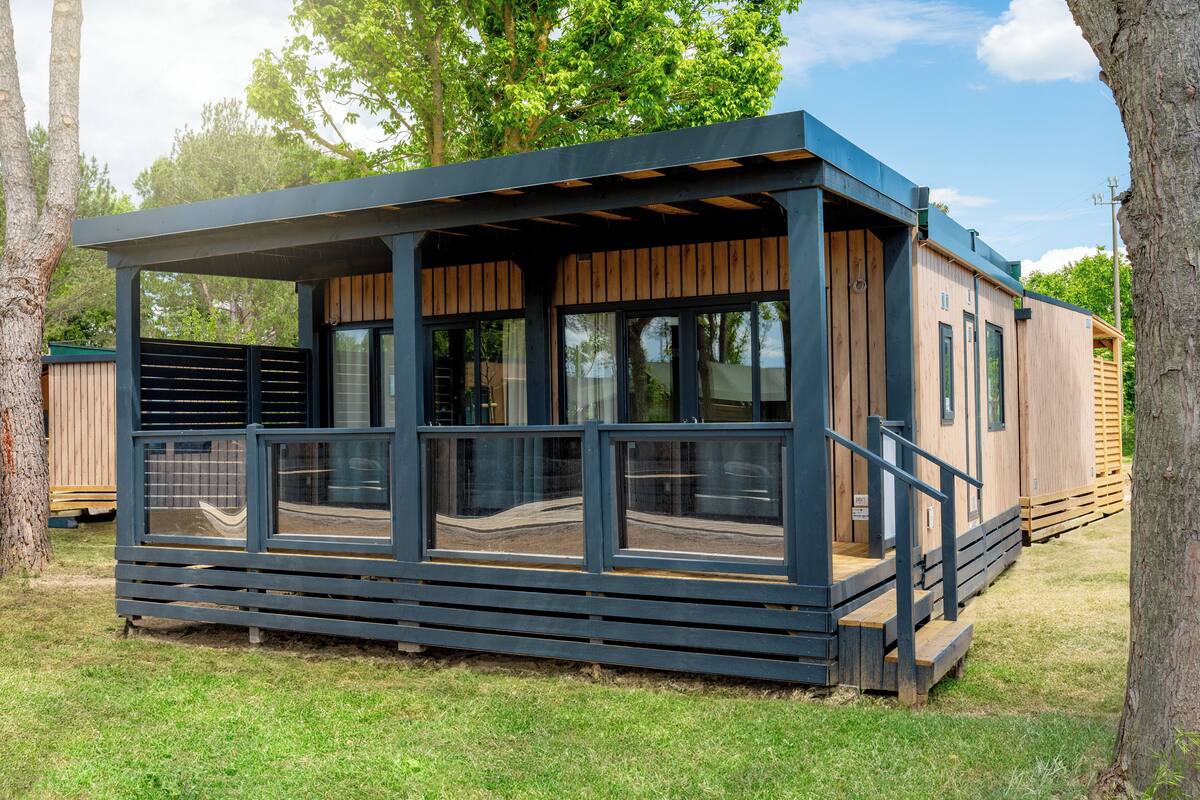Una cabaña moderna de madera con un porche cubierto y ventanas amplias.