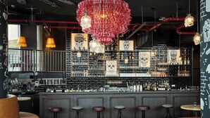 Een bar met een centraal bargedeelte, meerdere krukken en een decoratieve kroonluchter.