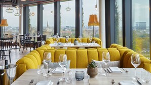 A restaurant with yellow upholstered seating, large windows, and a city view.