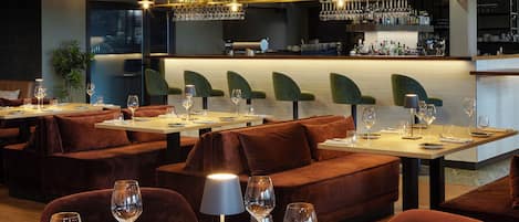 Ein Restaurant mit Samtboxsitzen, Tischen mit Weingläsern und einer Bar mit Flaschenregalen.