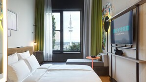 Een hotelkamer met een bed, een televisie, een tafeltje en een raam met uitzicht op een toren.