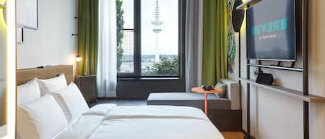 A hotel room with a bed, a TV, a small table, and a window with a view of a tower.