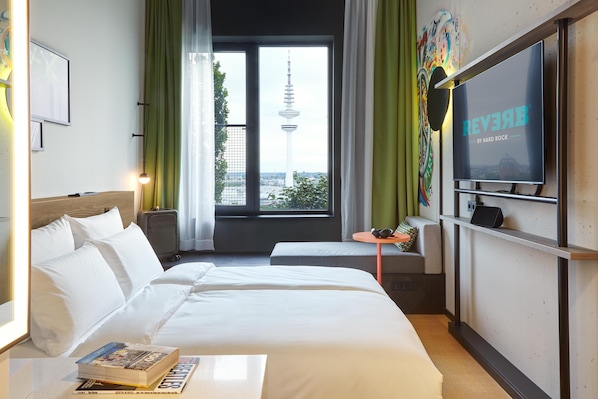 Habitación de hotel con cama, televisión, una mesita y ventana con vista a una torre.