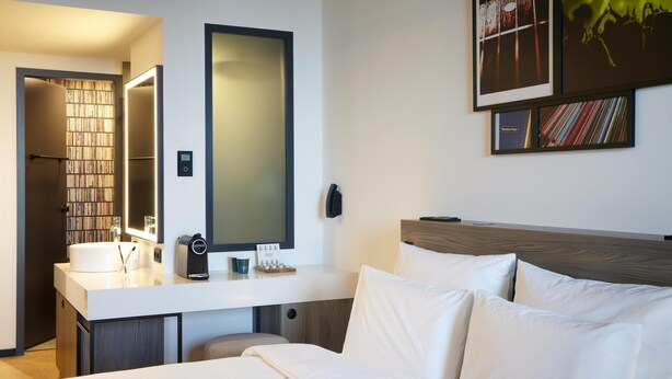 A hotel room with a bed, a bedside table with a lamp, a mirror, and a wall-mounted TV.