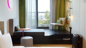 Een moderne hotelkamer met een groot raam, een bank, een klein rond tafeltje en een koffer.