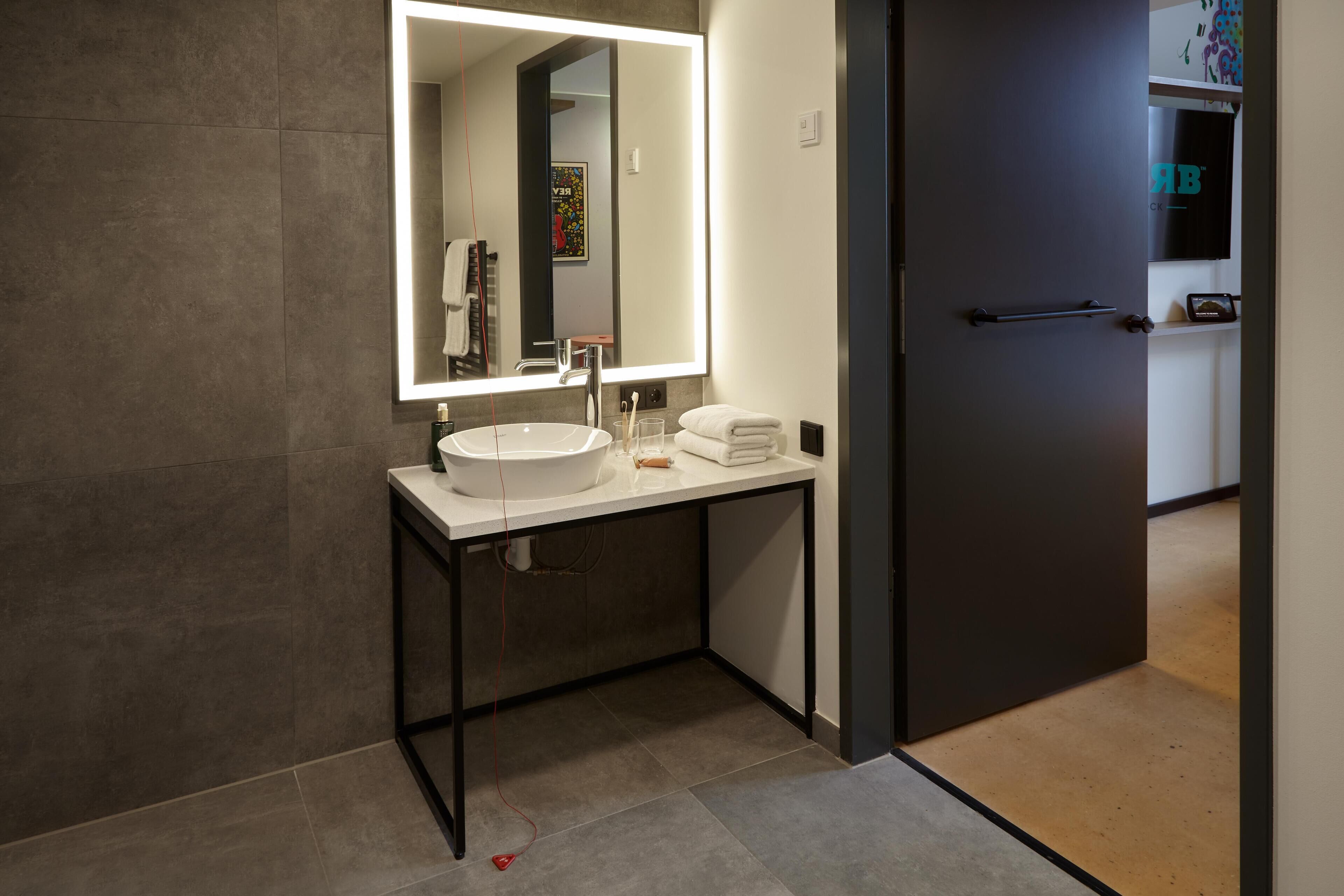 Un baño moderno con un espejo grande, un lavamanos blanco y un perchero para toallas.