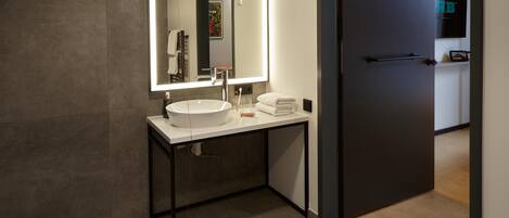 Un baño moderno con un espejo grande, un lavamanos blanco y un perchero para toallas.