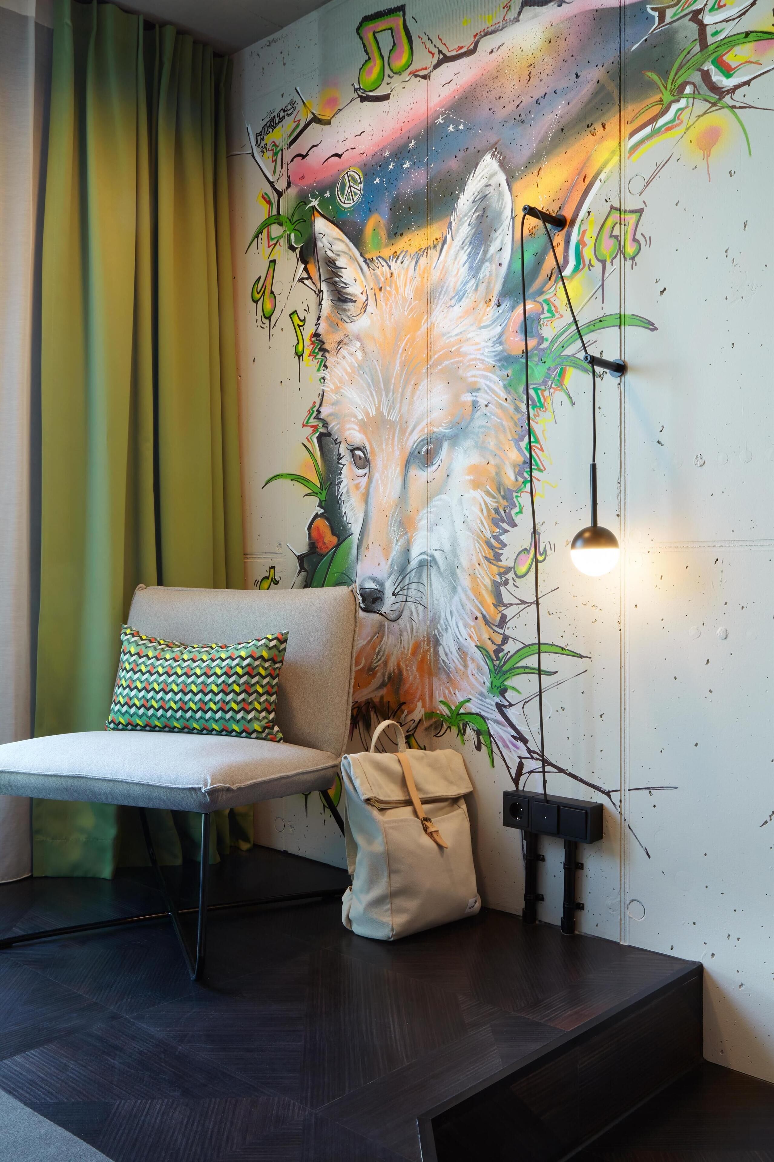 A room with a wall mural of a fox, a sofa with a patterned pillow, a small table, and a hanging light fixture.