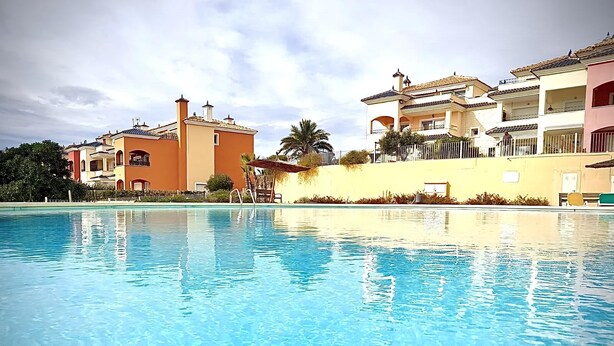 Una piscina con agua azul cristalina, rodeada de edificios con balcones y una palmera.