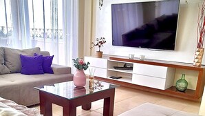 Una sala de estar moderna con un sofá beige, una mesa de centro de vidrio y un televisor de pantalla plana montado en la pared.