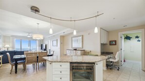 A modern kitchen with a granite countertop, white cabinetry, and a built-in oven. There is a dining area with a table and chairs, and a kitchen island with a sink. - Direct Oceanfront 3-bedroom 3 bath condo with direct beach access, fitness room, indoor and outdoor pool (Ocean City)