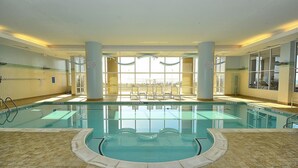 A large indoor swimming pool with clear water, surrounded by lounge chairs and a view of the beach through large windows. - Direct Oceanfront 3-bedroom 3 bath condo with direct beach access, fitness room, indoor and outdoor pool (Ocean City)