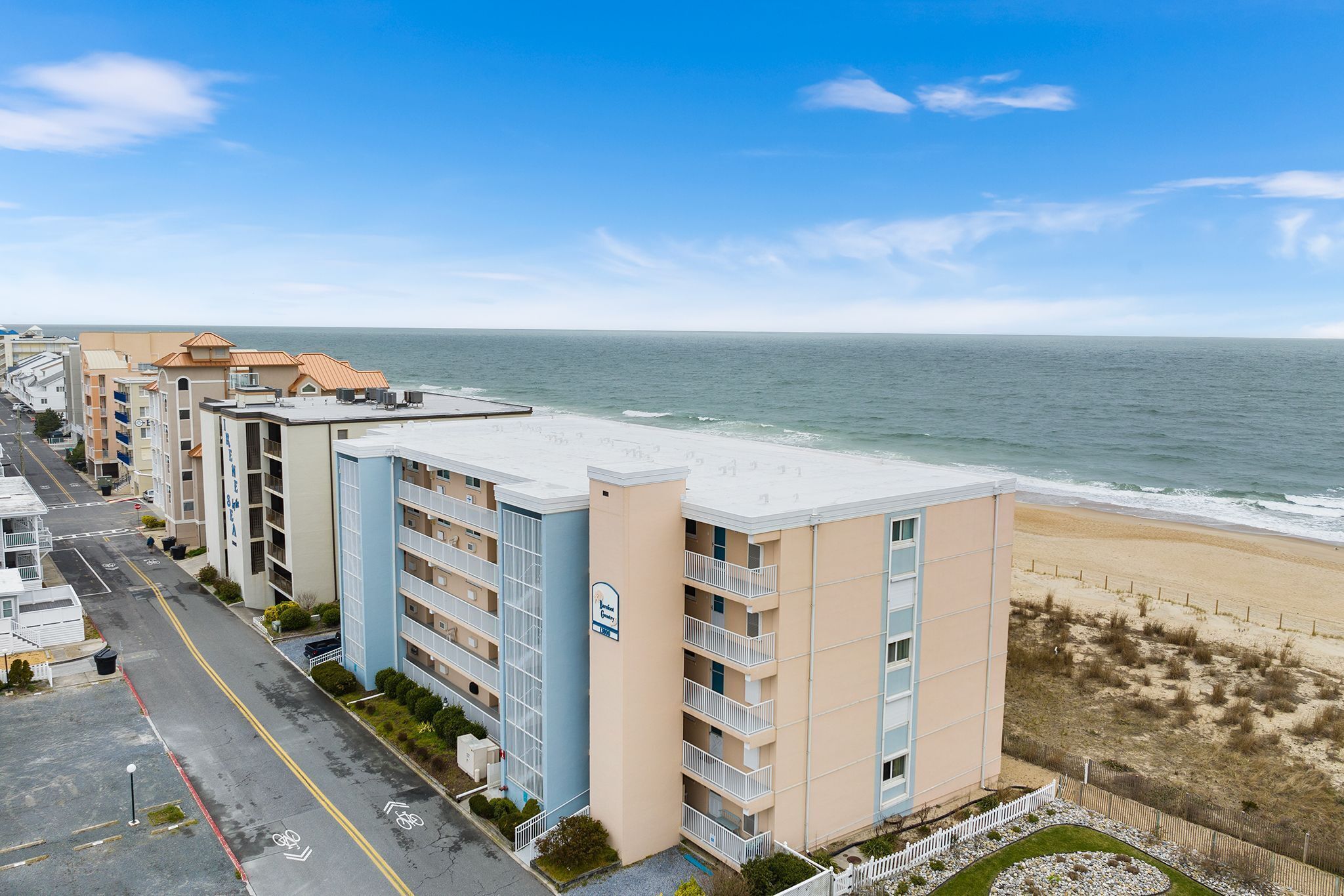 A beachfront hotel with multiple floors, a parking lot, and a view of the ocean.