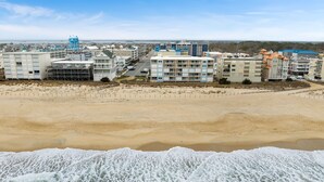 Et kysthotel med flere bygninger, en sandstrand og bølger der slår ind mod kysten.