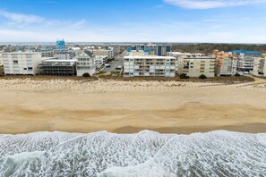 Un hôtel en bord de mer composé de plusieurs bâtiments, avec une plage de sable fin et des vagues qui se brisent sur le rivage.