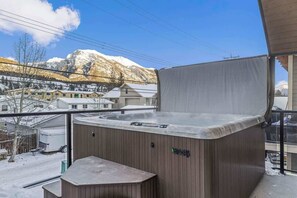 Una vasca idromassaggio su un balcone con vista su montagne innevate e un paese sullo sfondo.