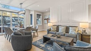 A spacious living room with a large window, a dining area, and a cozy seating arrangement. - NEW Schloss by SSR Top View HOT TUB 5BR ( BL# RES-11684 ) (Canmore)