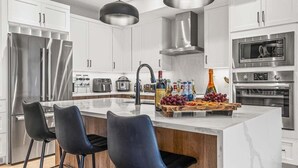 A modern kitchen with white cabinets, stainless steel appliances, and a marble island with bar stools. - NEW Schloss by SSR Top View HOT TUB 5BR ( BL# RES-11684 ) (Canmore)