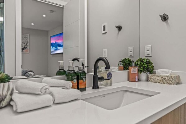 Un baño moderno con un espejo grande, un lavamanos con artículos de aseo y toallas.