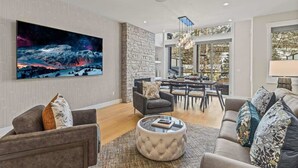 A modern living room with a large painting, a stone wall, and a dining area visible through glass doors. - NEW！ Chambord by SSR Top View HOT TUB 5BR ( BL# RES-11745 ) (Canmore)