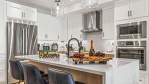 A modern kitchen with white cabinets, stainless steel appliances, a marble island, and black bar stools. - NEW！ Chambord by SSR Top View HOT TUB 5BR ( BL# RES-11745 ) (Canmore)