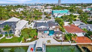 A residential area with a large house featuring a swimming pool, a dock with kayaks, and a view of the city skyline. - Waterfront w/Putting Green, Heated Pool, Dock -Manatee Cove (Lido Key)