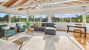 A spacious living room with a high ceiling, large windows, and a view of palm trees and buildings. - Waterfront w/Putting Green, Heated Pool, Dock -Manatee Cove (Lido Key)