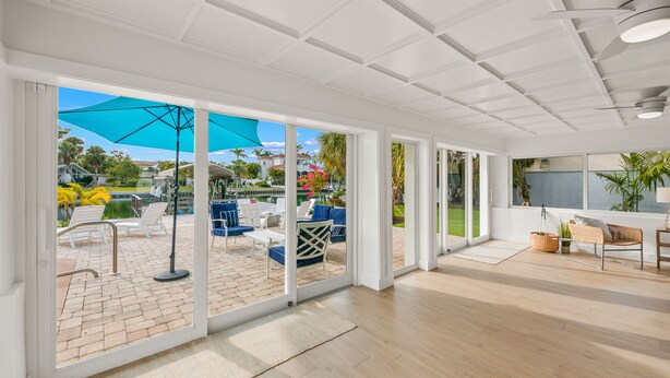 A spacious room with large windows, a wooden floor, and a view of an outdoor patio with chairs and umbrellas. - Waterfront w/Putting Green, Heated Pool, Dock -Manatee Cove (Lido Key)