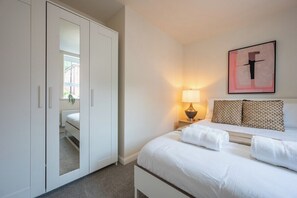 Ein Hotelzimmer mit Bett, Nachttisch mit Lampe, einem gerahmten Kunstwerk an der Wand und einem Kleiderschrank.
