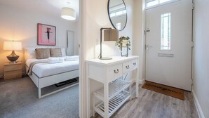 Ein Schlafzimmer mit Bett, Nachttisch, Lampe und einem an der Wand befestigten Spiegel.