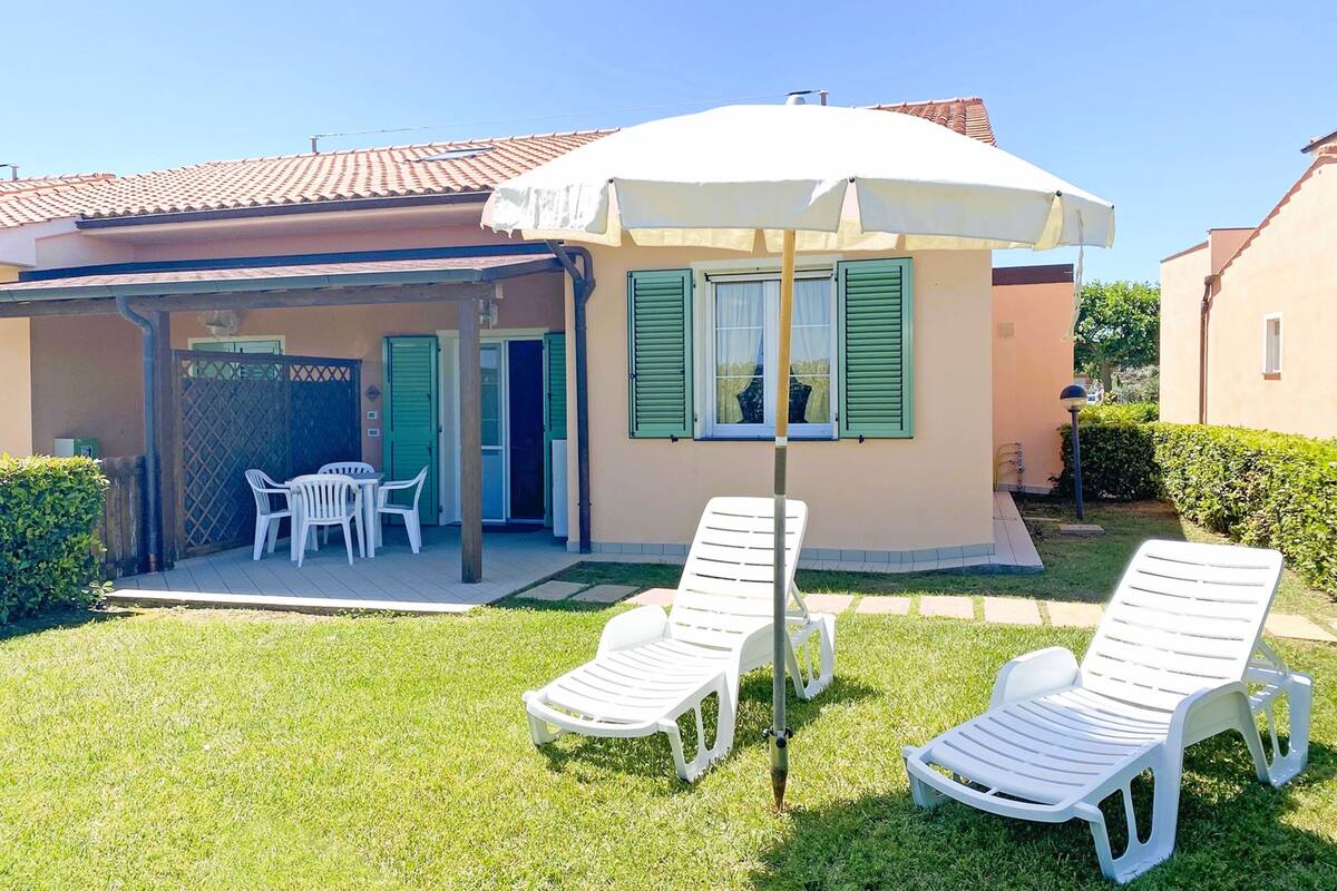 A house with a patio, two white lounge chairs, a table, and a white umbrella.