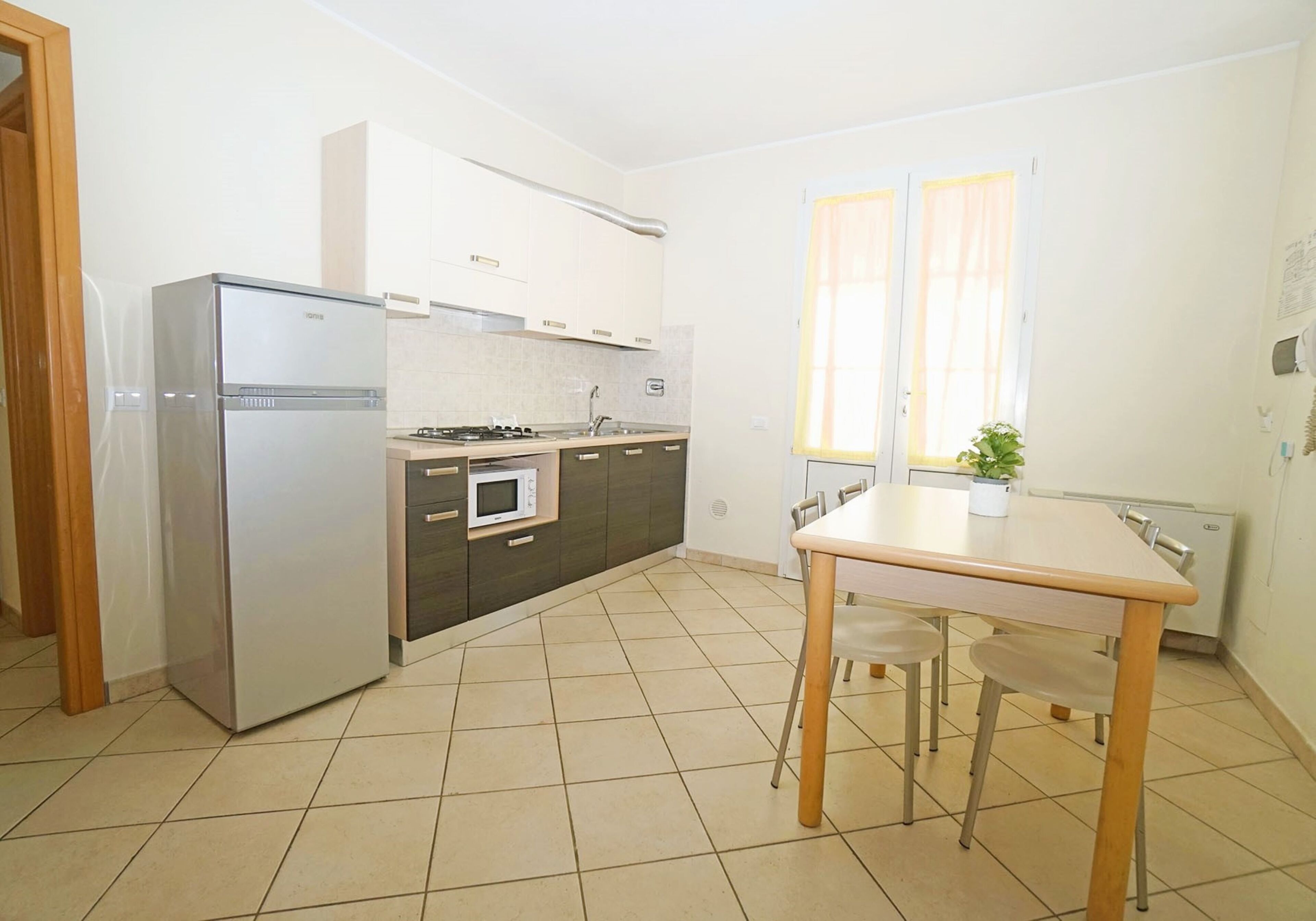 A modern kitchen with a refrigerator, microwave, stove, and cabinets. There is a dining table with chairs and a window with curtains.