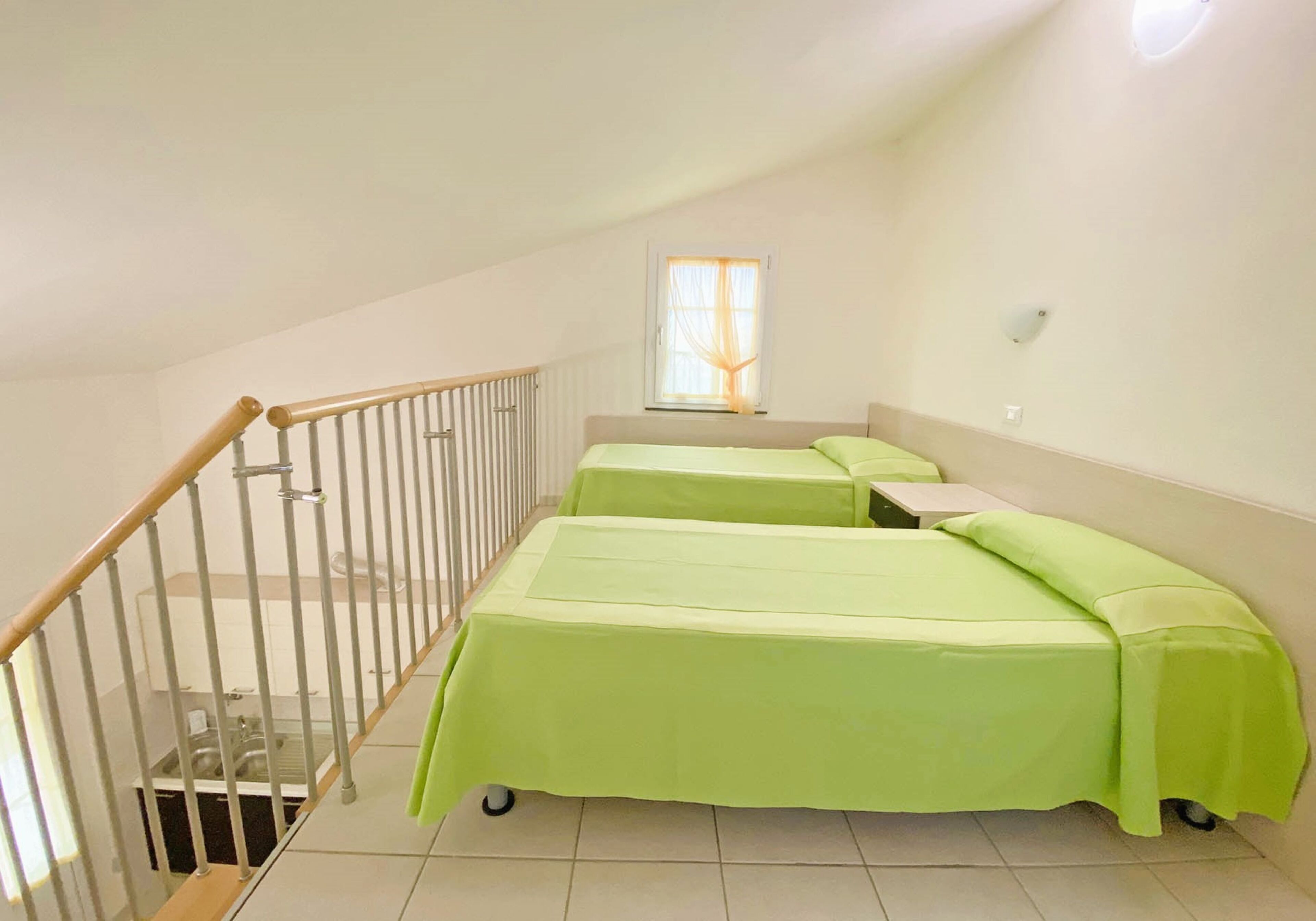 A room with two single beds, a wooden staircase, a window with curtains, and a radiator.