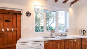 A kitchen with wooden cabinets, a white countertop, a built-in dishwasher, and a window with a view of trees. - 35 Main Street (Nottingham)