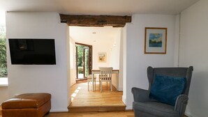 A living room with a wooden floor, a grey armchair with a blue pillow, a brown leather ottoman, a TV mounted on the wall, and a framed picture. - 35 Main Street (Nottingham)