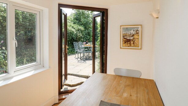 A room with a wooden table, a framed painting, and a view of an outdoor area with chairs and greenery. - 35 Main Street (Nottingham)