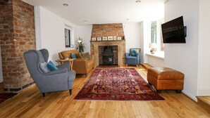 A spacious living room with a brick fireplace, wooden flooring, and a large rug. - 35 Main Street (Nottingham)