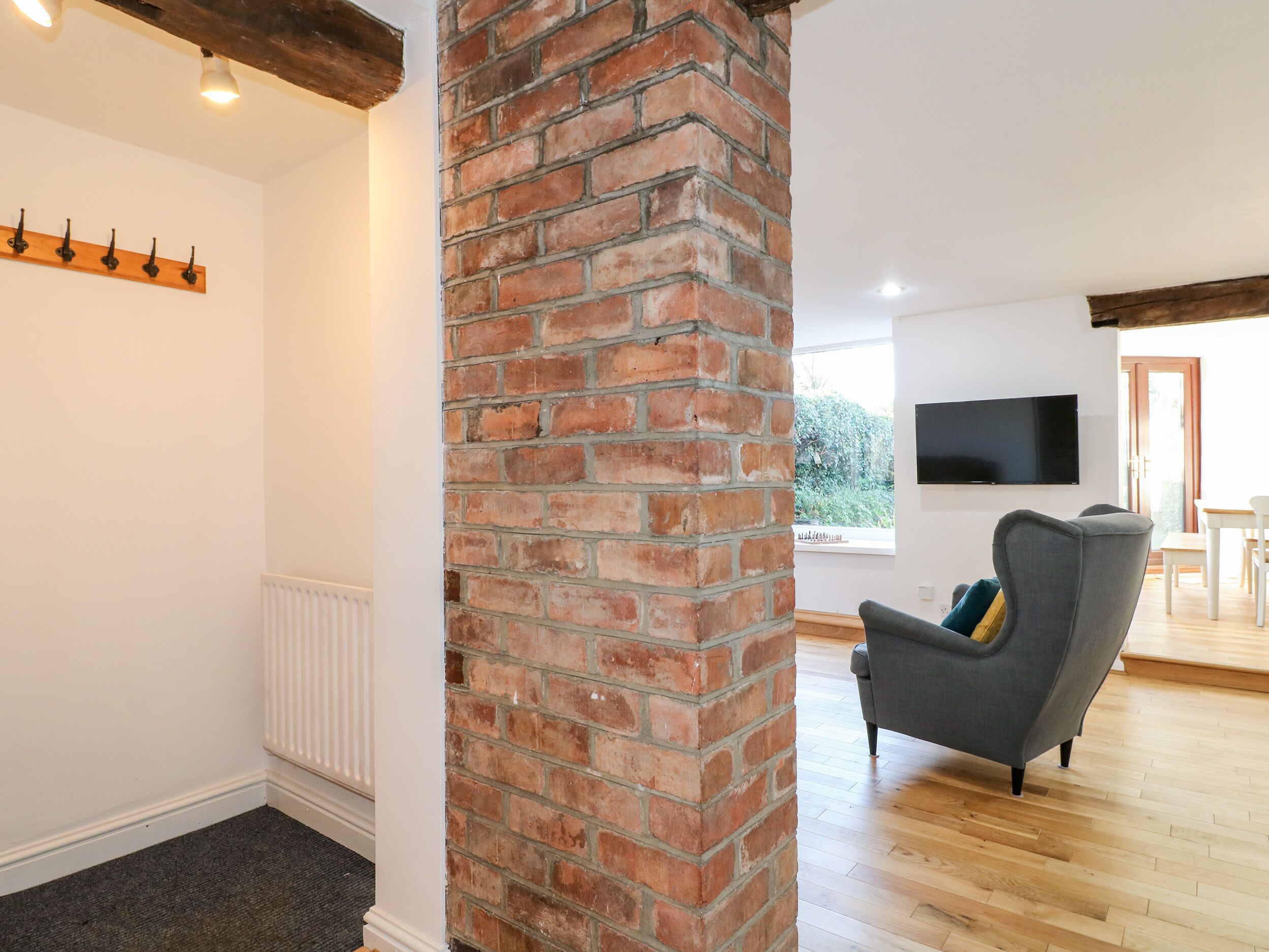 A living room with a brick fireplace, a grey armchair, a flat-screen TV, and a wooden floor.
