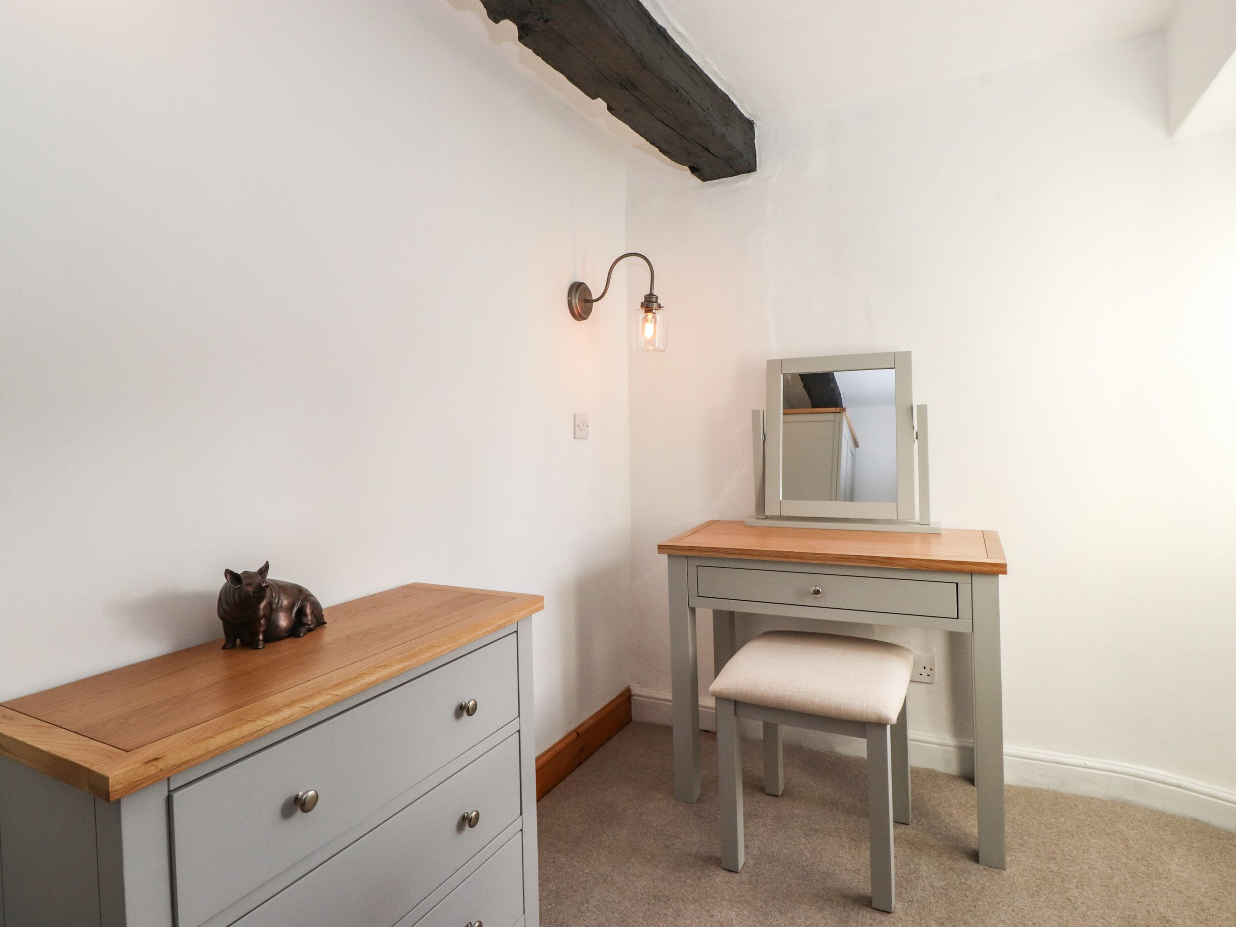 A small, well-lit room with a wooden desk, a chair, and a dresser.
