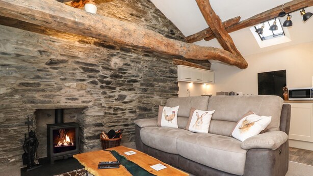 Una sala de estar acogedora con una chimenea de piedra, un sofá con cojines decorativos, una mesa de centro de madera y una cocina moderna al fondo.