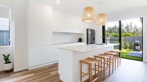 A modern kitchen with white cabinetry, a large island with bar stools, a built-in oven, and a view of the backyard.