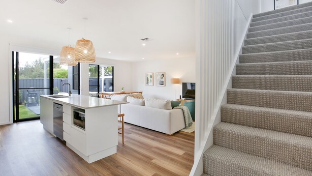 A modern kitchen with a central island, a dining area with a table and chairs, a sofa, and a staircase.