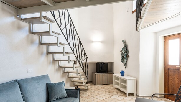 Una sala de estar con un sofá azul, una escalera, un televisor y una puerta de madera.