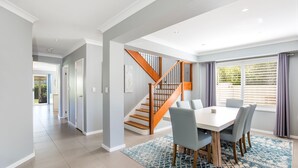 Un vaste espace dédié à la salle à manger, agrémenté d’un escalier en bois, d’une grande fenêtre avec des rideaux et offrant une vue sur la verdure environnante.