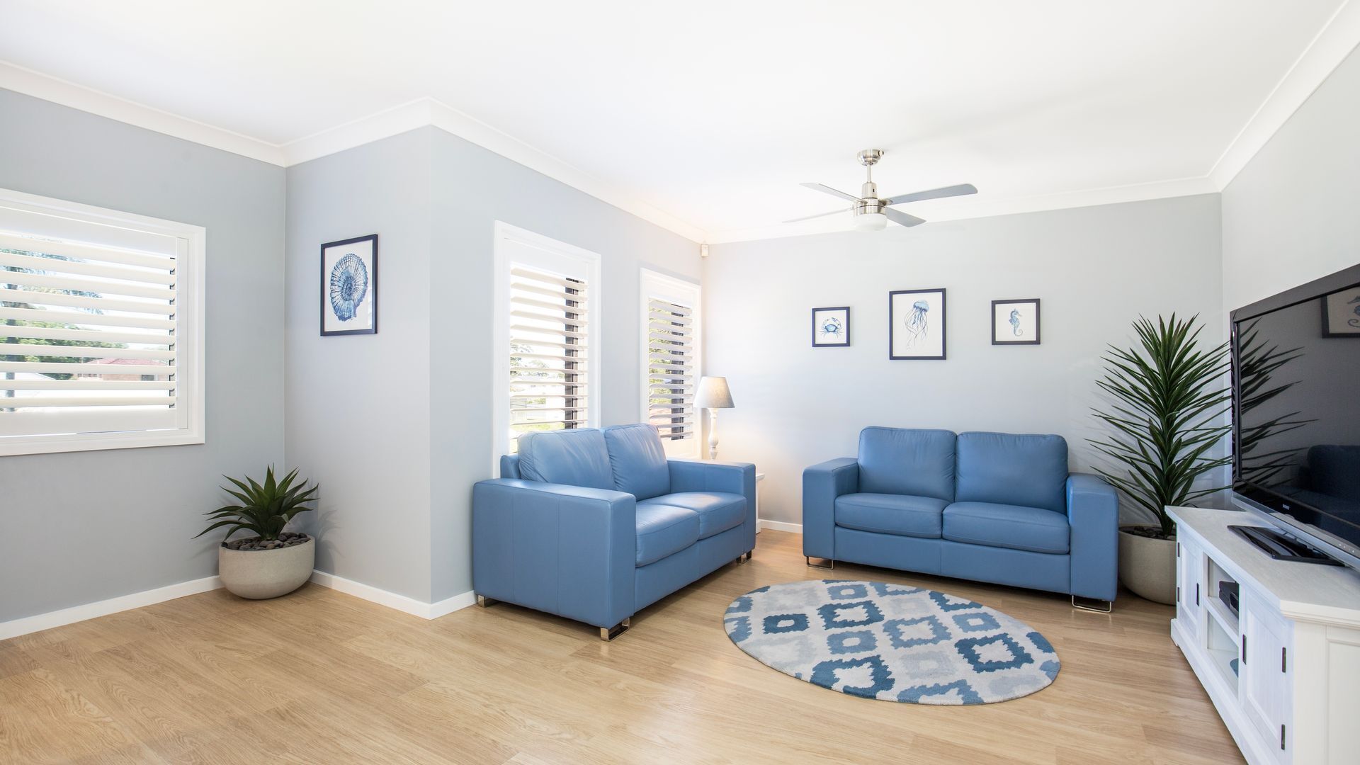 A modern living room with two blue sofas, a ceiling fan, and a TV stand.