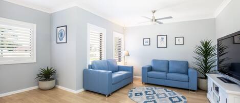 A modern living room with two blue sofas, a ceiling fan, and a TV stand.