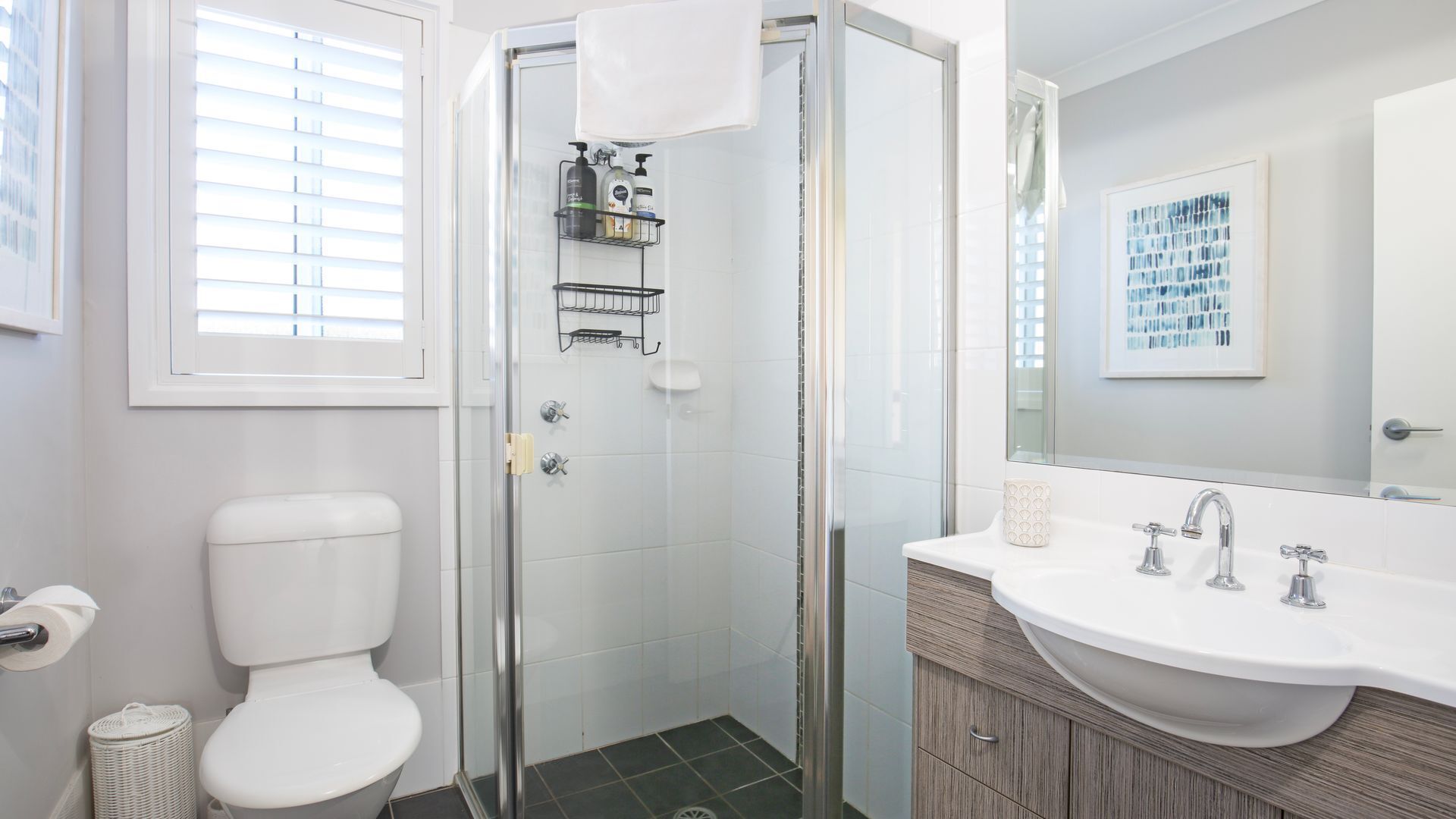 Une salle de bain moderne avec une douche à parois de verre, des toilettes blanches, un lavabo avec un miroir et une œuvre d’art encadrée accrochée au mur.